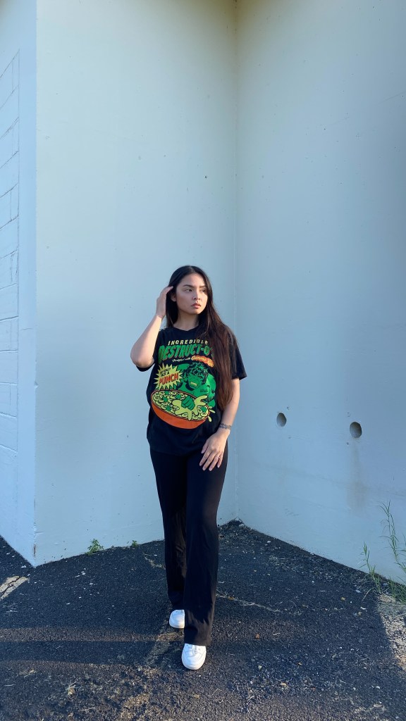 girl standing, looking to side, Hulk tee shirt, wide leg pants, Vans shoes 